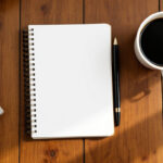 Open notebook and pen on a wooden table beside a cup of coffee in morning light