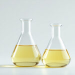Two laboratory flasks of different sizes holding pale golden essential oil side by side