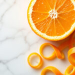 Halved Valencia orange with vivid pulp and a curl of zest on white marble